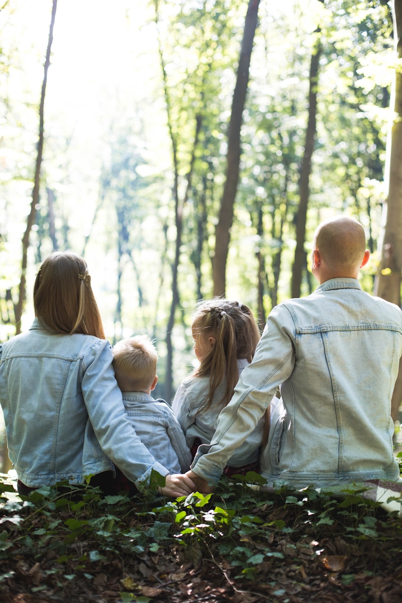 man and woman holding hands together with boy and girl looking at green trees during day life